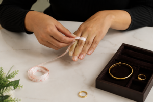 Woman measuring her finger and checking gold bangle and gold ring size at home using a measuring tape with gold jewellery on a table.